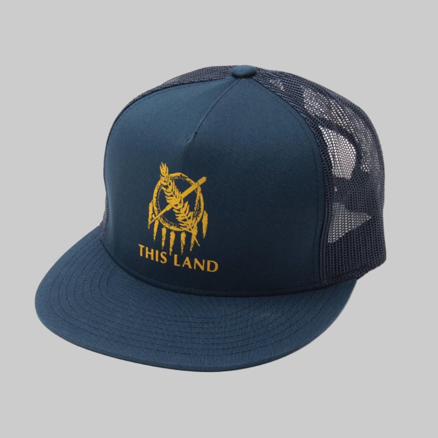 A navy blue trucker hat with a mesh back and an embroidered design of a snake eating its tail, with the text 'THIS LAND' underneath.