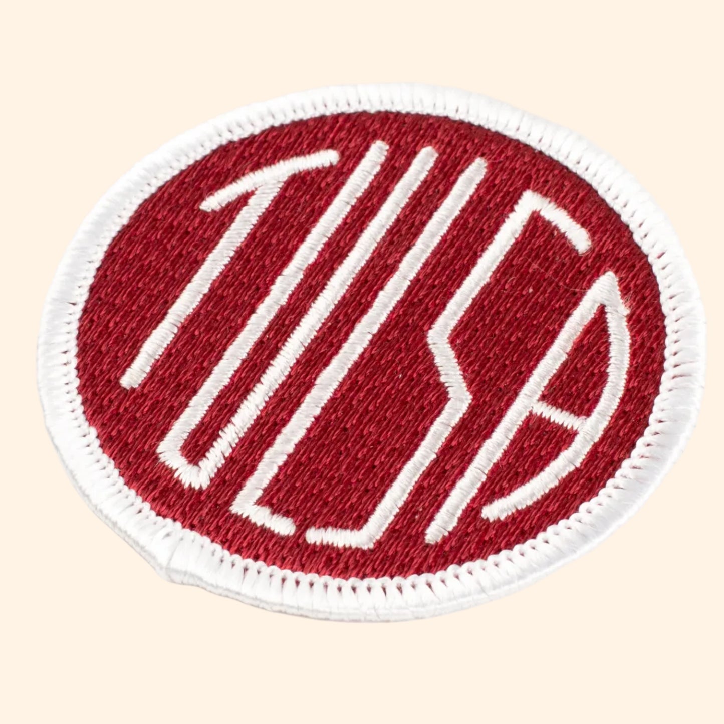 A red patch with a white TULSA text design, representing the Tulsa flag, with a marrowed edge and iron-on backing.